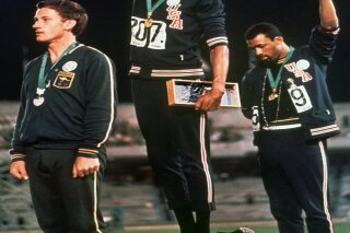 FILE - In this Oct. 16, 1968, file photo, extending gloved hands skyward in racial protest, U.S. athletes Tommie Smith, center, and John Carlos stare downward during the playing of the national anthem after Smith received the gold and Carlos the bronze for the 200 meter run at the Summer Olympic Games in Mexico City on. Australian silver medalist Peter Norman is at left. (AP Photo/File)