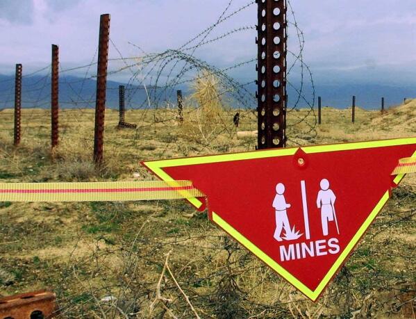 FILE - An international sign warning about mines hangs beside a minefield at Bagram Air Base on, March 22, 2002. The White House announced Tuesday a new policy curtailing the use of anti-personnel land mines by the U.S. military, reversing a more permissive stance that was enacted by former President Donald Trump. Under the policy, such explosives will still be allowed to defend South Korea against a potential attack by North Korea, but otherwise they will be banned.  (AP Photo/Mikhail Metzel, File)