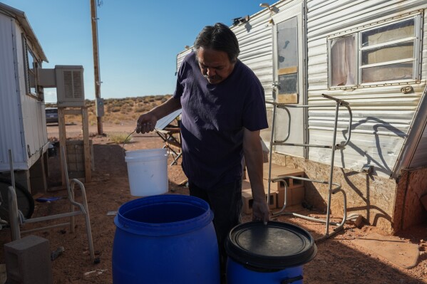 Ricky Gillis collects water for use in a evaporative air cooling unit, at left, Wednesday, Oct. 9, 2024, at his home on the Navajo Nation in Halchita, Utah. (AP Photo/Joshua A. Bickel)