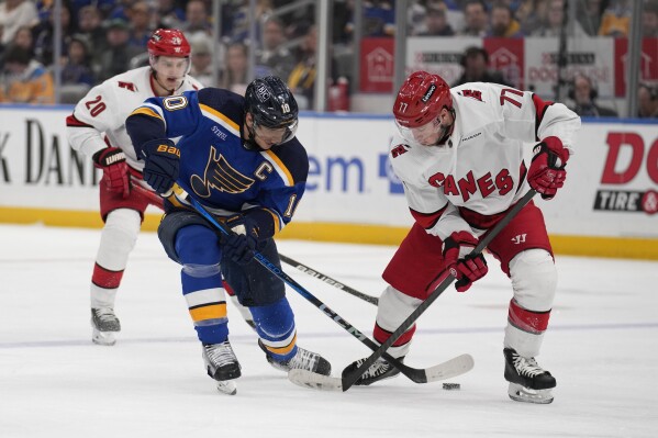 St. Louis Blues' Brayden Schenn (10) and Carolina Hurricanes' Tony DeAngelo (77) battle for a loose puck during the second period of an NHL hockey game Friday, April 12, 2024, in St. Louis. (AP Photo/Jeff Roberson)