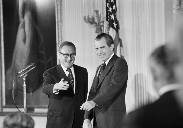 FILE - Secretary of State Henry Kissinger, left, gestures to the audience in the East Room of the White House, Sept. 22, 1973, as President Richard Nixon watches, in Washington. Kissinger had just been sworn in as the 56th secretary of state. Kissinger, the diplomat with the thick glasses and gravelly voice who dominated foreign policy as the United States extricated itself from Vietnam and broke down barriers with China, died Wednesday, Nov. 29, 2023. He was 100. (AP Photo, File)