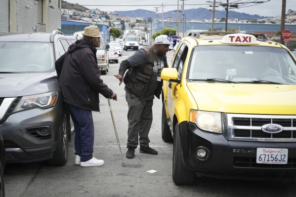 Ventrell Johnson, middle, of the San Francisco Homeless Outreach Team, helps call a taxi for Larry James Bell, a homeless resident who will be moving from temporary shelter into permanent housing Tuesday, Sept. 10, 2024, in San Francisco. (AP Photo/Terry Chea)