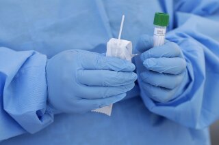 FILE - In this March 20, 2020, file photo, a health care worker prepares to collect a sample to test for COVID-19 at a drive-thru testing site in Miami. Thieves steal surgical masks. A clinic sells fake COVID-19 tests. Hate groups encourage sick members to infect law enforcement officers. Imposters pose as public health officials. As the coronavirus pandemic spreads across the globe so too do the crimes related to it. (AP Photo/Wilfredo Lee, File)