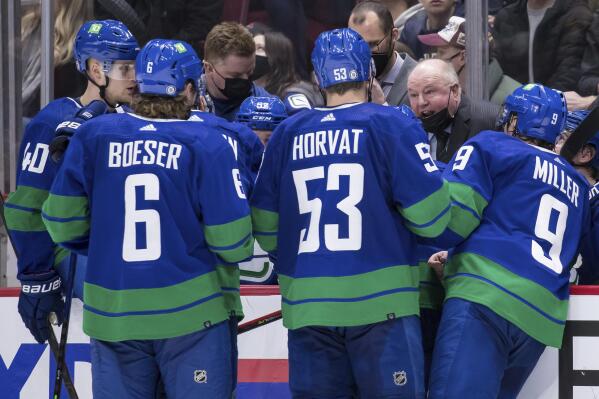 Vancouver Canucks head coach Bruce Boudreau, back right, talks to Elias Pettersson, of Sweden, from left to right, Brock Boeser, Bo Horvat and J.T. Miller during a timeout during the third period of an NHL hockey game  against the Columbus Blue Jackets Tuesday, Dec. 14, 2021 in Vancouver, British Columbia. (Darryl Dyck/The Canadian Press via AP)