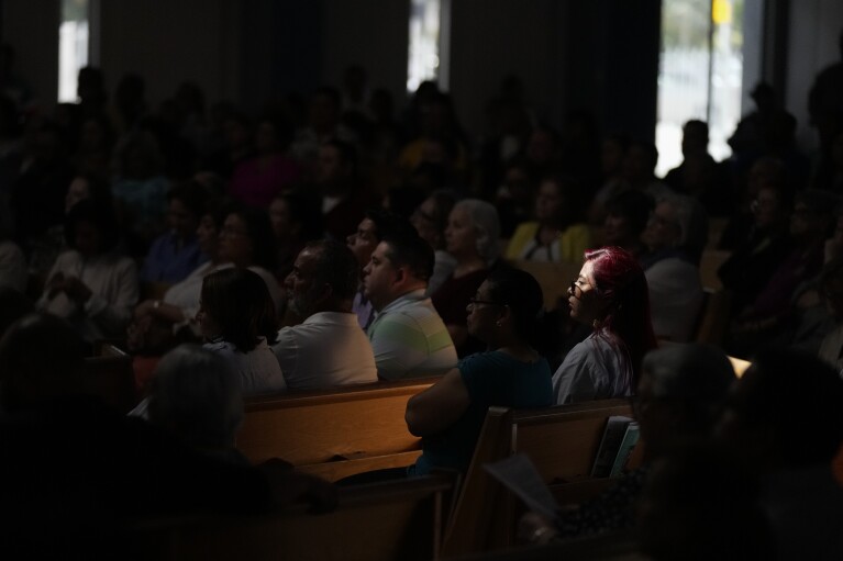 FILE - Cinthya Benavides, lit by a beam of light from a skylight, attends Mass at St. Agatha Catholic Church, a hub of Miami's Nicaraguan community, Sunday, Nov. 5, 2023, in Miami. Moves by the Nicaraguan government against young protesters and the church, where college student Benavides was active in youth ministry, pushed her to leave Nicaragua – fleeing her house with only her passport, phone and laptop as police knocked on the front door. (AP Photo/Rebecca Blackwell, File)