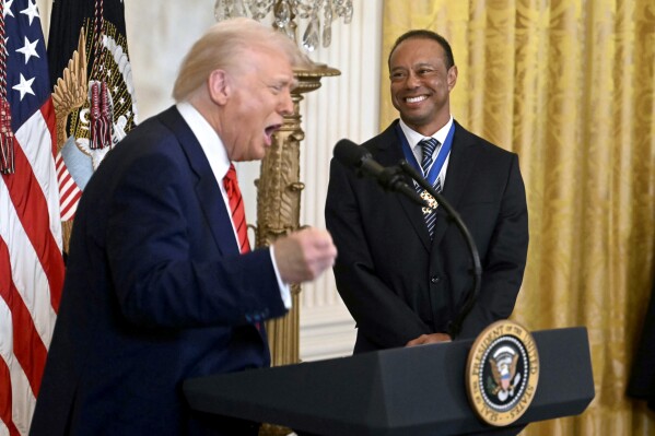 President Donald Trump speaks as golfer Tiger Woods listens during a reception for Black History Month in the East Room of the White House, Thursday, Feb. 20, 2025, in Washington. (Pool via AP)
