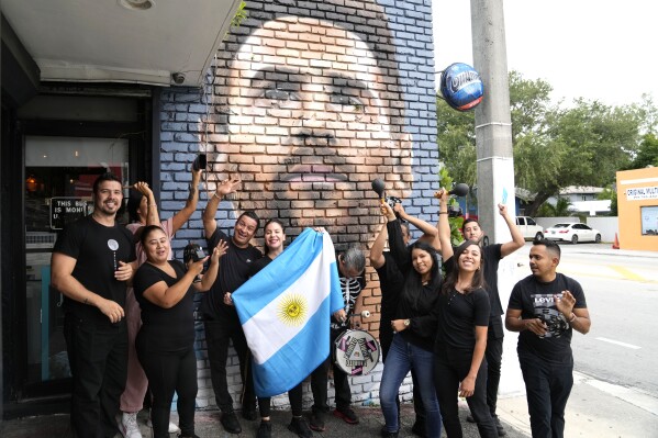 Staff at the Fiorito restaurant pose in front of a mural of Lionel Messi to celebrate after the Argentine soccer star announced he is joining the Major League Soccer team Inter Miami, Wednesday, June 7, 2023, in Miami. Murals, burgers, beers, and billboards are just a handful of examples that show the euphoria that Messi generates in South Florida and how he will be received. (AP Photo/Lynne Sladky)