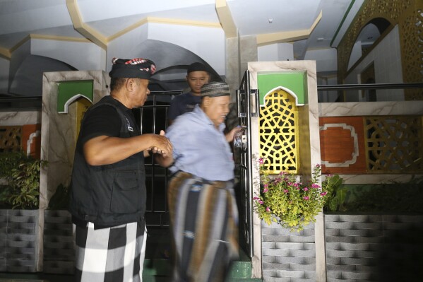 A traditional Balinese guard, known as Pecalang, helps an elderly Muslim man leave a mosque with minimal light just to assist worshippers home on Nyepi, the day of silence, which also coincided with the first day of Ramadan in Tuban village, Bali, Indonesia on Monday, March 11, 2024. Airports closed for 24 hours, the internet was turned off and streets were empty as the predominantly Hindu island of Bali in Muslim-majority Indonesia marked its New Year with an annual Day of Silence, part of six days of extensive New Year rituals. (AP Photo/Firdia Lisnawati)