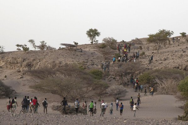 In this July 15, 2019 photo, Ethiopian migrants are led by a smuggler to a disembarking point on the uninhabited coast outside the town of Obock, Djibouti, on the shore closest to Yemen. Long lines of migrants descend single file down mountain slopes to the rocky coastal plain, where many lay eyes on the sea for first time, and eventually board the boats. (AP Photo/Nariman El-Mofty)