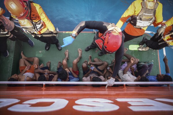Members of Indonesia's National Search and Rescue Agency give instructions to Rohingya refugees rescued from a capsized fishing boat off West Aceh, Indonesia, on Thursday, March 21, 2024. The wooden fishing boat carried about 140 Rohingya refugees, but only 75 people were rescued. In interviews with The Associated Press, eight of the survivors described abuses on board the fishing boat. (AP Photo/Reza Saifullah)