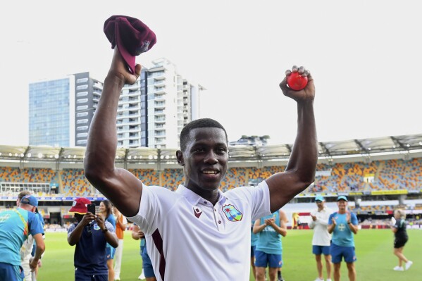 West Indies' Shamar Joseph raises the ball after taking 7 wickets in his team's defeat of Australia on the 4th day of their cricket test match in Brisbane, Sunday, Jan. 28, 2024. (Jono Searle/AAP Image via AP)