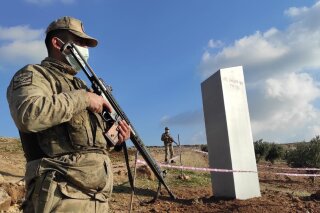 Turkish police officers guard a monolith, found on an open field near Sanliurfa, southeastern Turkey, Sunday, Feb. 7, 2021. The metal block was found by a farmer Friday in Sanliurfa province with old Turkic script that reads "Look at the sky, see the moon." The monolith, 3 meters high (about 10 feet), was discovered near UNESCO World Heritage site Gobeklitepe with its megalithic structures dating back to 10th millennium B.C. Turkish media reported Sunday that gendarmes were looking through CCTV footage and investigating vehicles that may have transported the monolith. Other mysterious monoliths have popped up and some have disappeared in numerous countries since 2020. (Bekir Seyhanli/IHA via AP)