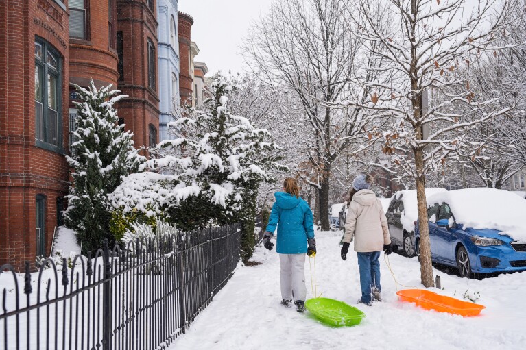 Girls walk through the Capitol Hill neighborhood dragging sleds, Friday, Jan. 19, 2024, as school was cancelled due to snow in Washington. (AP Photo/Jacquelyn Martin)