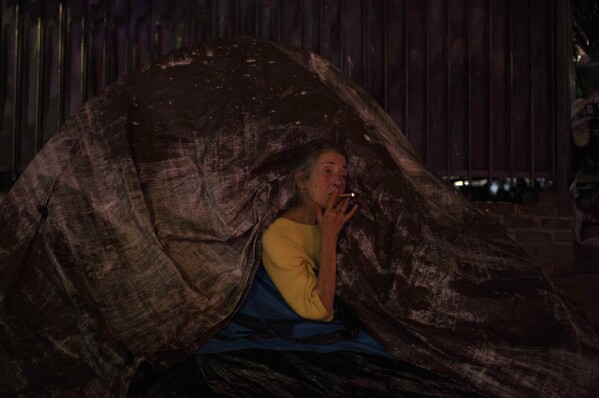 Patricia Sweeney smokes a cigarette through a small gap in her tent as her partner sleeps inside the tent in Los Angeles Tuesday, Oct. 17, 2023. (AP Photo/Jae C. Hong)