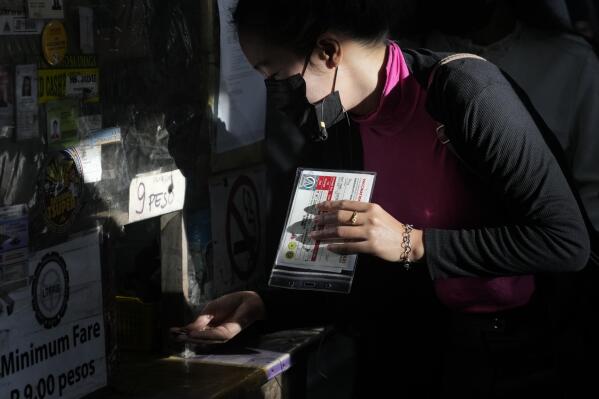 A woman shows her vaccination card before riding a passenger jeep at a terminal in Quezon city, Philippines on Monday, Jan. 17, 2022. People who are not fully vaccinated against COVID-19 were banned from riding public transport in the Philippine capital region Monday in a desperate move that has sparked protests from labor and human rights groups. (AP Photo/Aaron Favila)
