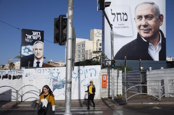 FILE - In this March. 1, 2020 file photo, people walk next to election campaign billboards showing Israeli Prime Minister Benjamin Netanyahu, right, and Benny Gantz, left, in Bnei Brak, Israel. Israel’s president on Sunday, April 12, 2020, turned down a request from Blue and White party leader Benny Gantz for a two-week extension to form a new coalition government. The announcement means that Gantz and Netanyahu have a midnight deadline on Monday night to reach a power-sharing deal. If they fail, the country could be forced into a fourth consecutive election in just over a year. (AP Photo/Oded Balilty, File)