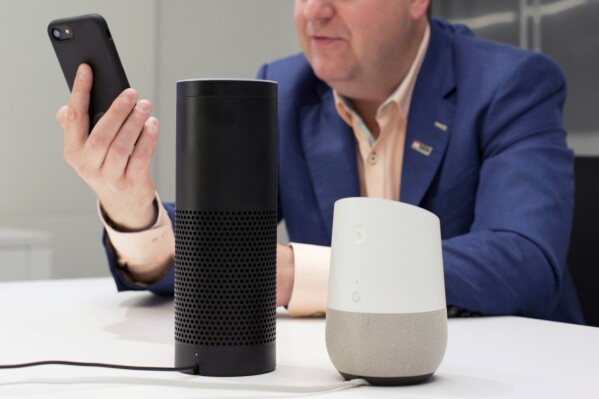 A man holds an iPhone next to an Amazon Echo, center, and a Google Home, right, in New York on June 14, 2018. A study published Monday, Aug. 28, 2023, in JAMA Network Open, says Alexa, Siri and other voice assistants could do a better job giving instructions on CPR to help bystanders respond in emergencies. (AP Photo/Mark Lennihan)