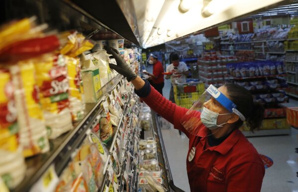 Maclola Orozco wears protective gear as a precaution against the coronavirus as she restocks shelves at El Rancho grocery store in Dallas, Monday, April 13, 2020. (AP Photo/LM Otero)