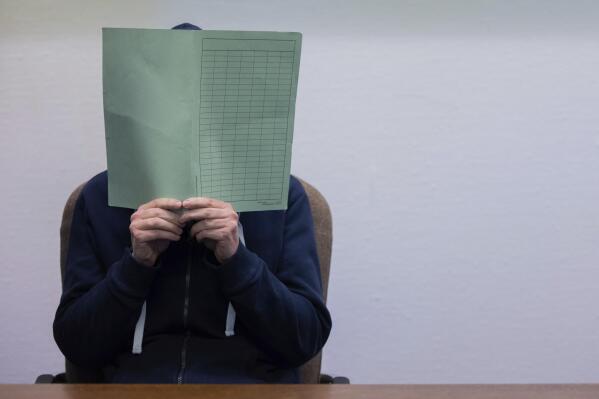 The defendant in the Wermelskirchen abuse complex holds a folder in front of his face in the courtroom in Cologne, Tuesday, Feb. 28, 2023. A 45-year-old German man who had offered babysitting services online has been convicted of sexually abusing children. The case shocked even veteran investigators and led them to uncover numerous other abuse suspects. The regional court in Cologne on Tuesday sentenced the defendant, whose name wasn’t released for privacy reasons, to 14 years and six months in prison. (Rolf Vennenbernd/dpa via AP)