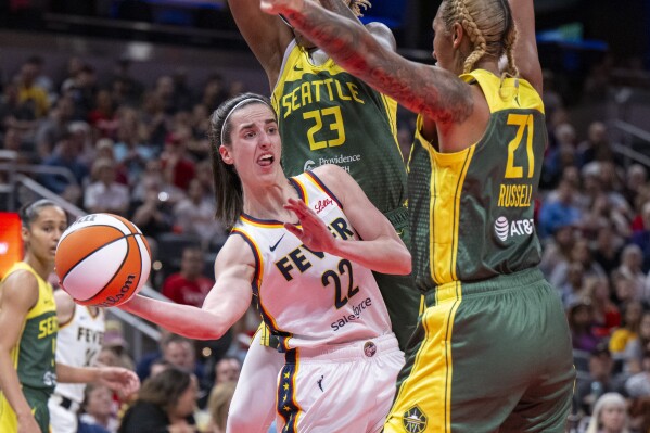 FILE - Indiana Fever guard Caitlin Clark (22) passes the ball from under the basket while being defended by Seattle Storm guard Jordan Horston (23) and center Mercedes Russell (21) during the first half of a WNBA basketball game Thursday, May 30, 2024, in Indianapolis. (AP Photo/Doug McSchooler, File)