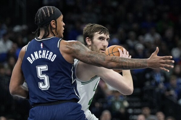 Boston Celtics' Luke Kornet, right, looks to pass the ball as he is guarded by Orlando Magic's Paolo Banchero (5) during the first half of an NBA basketball game, Friday, Nov. 24, 2023, in Orlando, Fla. (AP Photo/John Raoux)