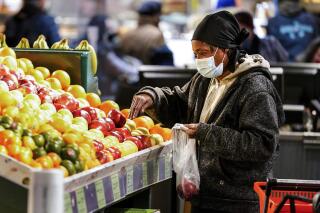 A shopper waring a proactive mask as a precaution against the spread of the coronavirus selects fruit at the Reading Terminal Market in Philadelphia, Wednesday, Feb. 16, 2022.  The majority of healthy Americans, including students in schools, can safely take a break from wearing masks under new U.S. guidelines released Friday, Feb. 25. The Centers for Disease Control and Prevention outlined a new set of measures for communities where COVID-19 is easing its grip, with less of a focus on positive test results and more on what’s happening at hospitals. (AP Photo/Matt Rourke)