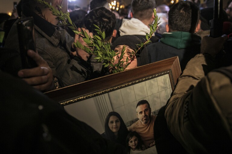 A woman holds a photo of her relatives, victims of the catastrophic earthquake that struck the country during the first anniversary of the quake, in the city of Antakya, southern Turkey, Tuesday, February 6, 2024. (AP Photo/Metin Yuksu)