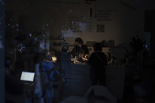 A barman is seen working through the window of a coffee shop during power cuts in Kyiv, Ukraine, Friday, June 7, 2024. Ukraine, including Kyiv, is struggling to cope with a new wave of rolling blackouts after relentless Russian attacks took out half the country’s power generation capacity. (AP Photo/Alex Babenko)