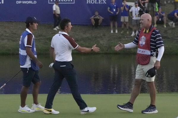 Europe's Rory Mcilroy, centre, goes to shake hands with United States' Patrick Cantlay 's caddie Joe LaCava, on the 18th green following the end of during the afternoon Fourballs matches at the Ryder Cup golf tournament at the Marco Simone Golf Club in Guidonia Montecelio, Italy, Saturday, Sept. 30, 2023. (AP Photo/Alessandra Tarantino)