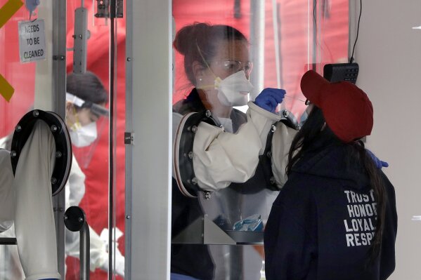 A medical worker, center, takes a sample from the nose of a woman at a coronavirus testing tent outside MGH Healthcare Center, Monday, April 20, 2020, in Chelsea, Mass. (AP Photo/Steven Senne)