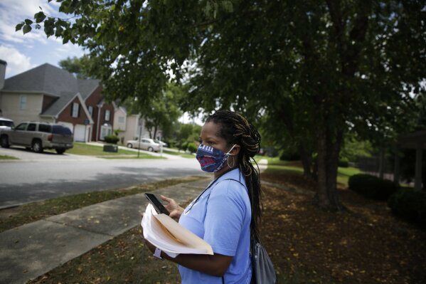 Audrey Allen, 54, walks on the sidewalk near a neighborhood where she hands out early voting registration forms on Wednesday, July 8, 2020, in Powder Springs, Ga. (AP Photo/Brynn Anderson)