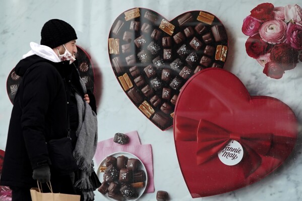 FILE - A man passes a Fannie May chocolate shop in downtown Chicago on Valentine's Day, Feb. 14, 2021. Valentine's Day is meant to celebrate romance and the depths of feeling we have for loved ones. So it may be surprising how much Valentine's shopping is done at the last minute. (AP Photo/Nam Y. Huh, File)