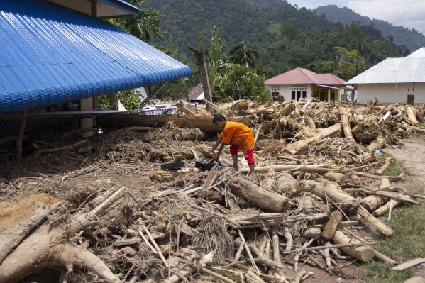 A boy crawls on logs swept into a neighborhood affected by a flash flood in Pesisir Selatan, West Sumatra, Indonesia, Wednesday, March 13, 2024. In Indonesia, environmental groups continue to point to deforestation and environmental degradation worsening the effects of natural disasters such as floods, landslides, drought and forest fires. (AP Photo/Mavendra JR)