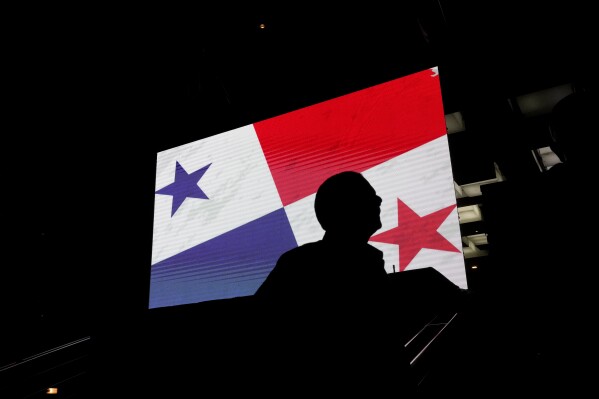 A supporter of Achieving Goals presidential candidate Jose Raul Mulino stands near a screen of a Panamanian flag outside his campaign headquarters as he waits for general election results in Panama City, Sunday, May 5, 2024. (AP Photo/Matias Delacroix)