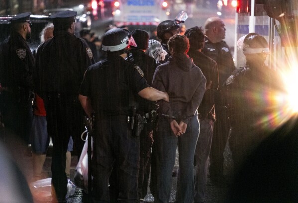 As light rain falls, New York City police officers take people into custody near the Columbia University campus in New York, Tuesday, April 30, 2024, after a building taken over by protesters earlier in the day was cleared, along with a tent encampment. (AP Photo/Craig Ruttle)