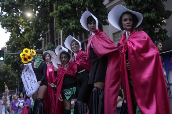 Women in red cloaks and white bonnets, dressed like the characters from the novel-turned-TV series "The Handmaid's Tale", mark International Women's Day in Rio de Janeiro, Brazil, Friday, March 8, 2024. (AP Photo/Silvia Izquierdo)