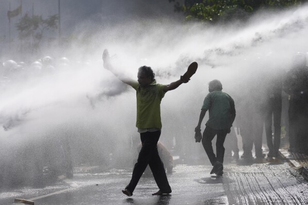 A supporter of Sri Lanka's main opposition holds his shoes in hands as police fire water cannons to disperse them during a protest rally against high taxes and increases in electricity and fuel charges, in Colombo, Sri Lanka, Jan. 30, 2024. (AP Photo/Eranga Jayawardena)