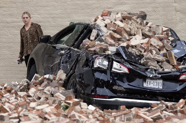 A woman looks at the damage caused by fallen bricks from a building wall in the aftermath of a severe thunderstorm Friday, May 17, 2024, in Houston, after thunderstorms pummeled southeastern Texas on Thursday. (AP Photo/David J. Phillip)