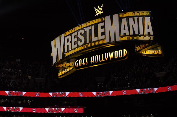 FILE - A WrestleMania sign hangs over the crowd during the WWE Monday Night RAW event, Monday, March 6, 2023, in Boston. WWE is flexing its branding muscle, selling more than 90,000 tickets to next year's WrestleMania about eight months before the premium live event is held and before a single match has been announced. (AP Photo/Charles Krupa, FIle)