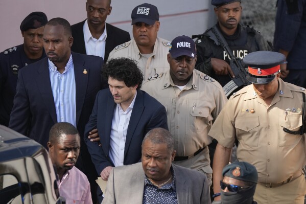 FILE - FTX founder Sam Bankman-Fried, center left, is escorted out of Magistrate Court following a hearing in Nassau, Bahamas, Dec. 19, 2022. Bankman-Fried, charged with a host of financial crimes, was arrested in the Bahamas on Dec. 12, 2022. (AP Photo/Rebecca Blackwell, File)