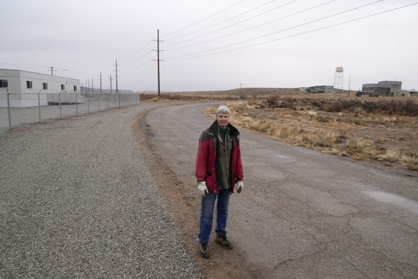 Gayna Salinas stands near a trailer, left, on land owned by Anson Resources, and a defunct uranium mine, right, Thursday, Jan. 25, 2024, in Green River, Utah.  (AP Photo/Brittany Peterson)