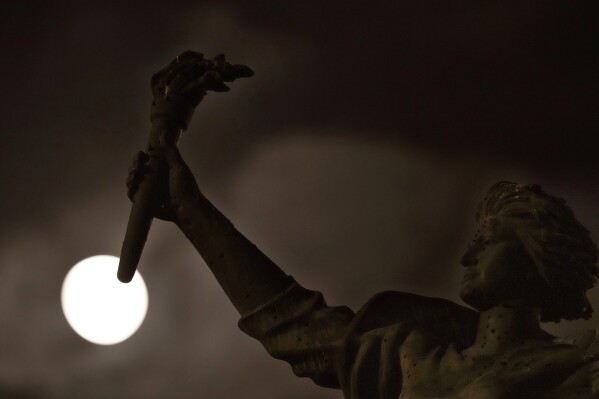The full moon rises beyond the Martyrs statue, in downtown Beirut, Lebanon, Wednesday, Aug. 30, 2023. (AP Photo/Hussein Malla)