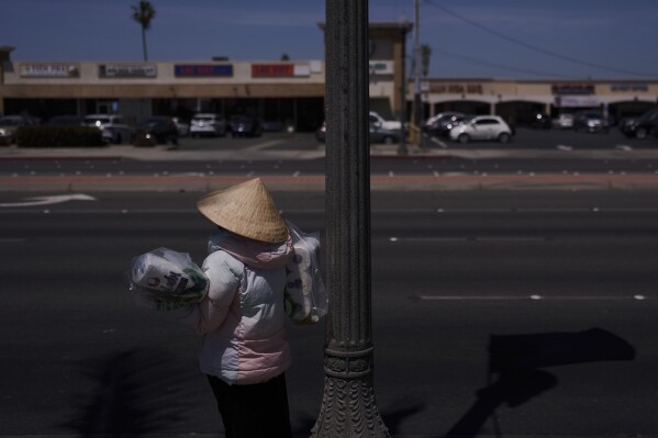 A woman wearing a traditional Vietnamese conical hat waits for a bus in the Little Saigon neighborhood of Westminster, Calif., Tuesday, April 22, 2025. (AP Photo/Jae C. Hong)