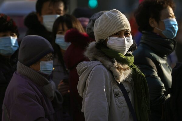 Commuters wearing face masks to help curb the spread of the coronavirus wait for their buses at a bus stand in Beijing, Thursday, Dec. 10, 2020. (AP Photo/Andy Wong)