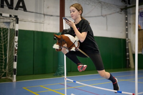 A girl jumps during a training session at a Hobby horsing competition in St. Petersburg, Russia, on Sunday, April 21, 2024. Several dozen kids, 48 girls and one boy, from first-graders to teenagers gathered in a gymnasium in northern St. Petersburg, Russia's second largest city, for a hobby horsing competition. (AP Photo/Dmitri Lovetsky)