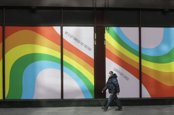 A man wearing a face mask to protect against catching the coronavirus walks past a window display of rainbows in the windows of the famous London department store Harrods in London, Tuesday, March 31, 2020. Rainbows in windows are being used to show hope in the fight against Covid-19, they were first used in Italy with the message 'Tutto andra' bene," or "Everything will turn out OK,", the Harrods version reads 'We'llGet Through This Together- Sunnier Days Ahead. (AP Photo/Kirsty Wigglesworth)