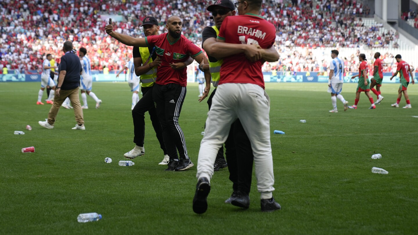 Stewards catch pitch invaders during the men's Group B soccer match between Argentina and Morocco at Geoffroy-Guichard Stadium at the 2024 Summer Olympics, Wednesday, July 24, 2024, in Saint-Etienne, France. (AP Photo/Silvia Izquierdo)