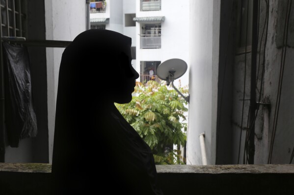 Rohingya child bride, D, age 13, stands next to a window in the hallway of an apartment complex in Kuala Lumpur, Malaysia, on Oct. 5, 2023. D came to Malaysia from Bangladesh in 2023 for an arranged marriage with an older man. During the journey, she says she was forced to eat jungle plants to survive and watched helplessly as a trafficker raped at least six other girls. Now in Malaysia, she says her husband forces her to have sex with him. (AP Photo/Victoria Milko)