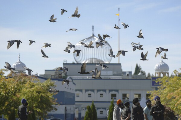 FILE - A flock of birds flies past as Moninder Singh, foreground right, a spokesperson for the British Columbia Gurdwaras Council (BCGC), waits to speak to reporters outside the Guru Nanak Sikh Gurdwara Sahib in Surrey, British Columbia, Canada, on Monday, Sept. 18, 2023, where temple president Hardeep Singh Nijjar was gunned down in his vehicle while leaving the temple parking lot in June. Canada expelled a top Indian diplomat Monday as it investigates what Prime Minister Justin Trudeau called credible allegations that India's government may have had links to the assassination in Canada of a Sikh activist. (Darryl Dyck/The Canadian Press via AP, File)