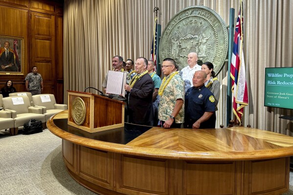 Hawaii officials stand behind Gov. Josh Green as he announces Wildfire Mitigation and Risk Reduction Preparedness Month in Honolulu on Friday, May 10, 2024. Green warns of a dry season as the state looks to prevent another wildfire like the one in August that burned the town of Lahaina and killed 101 people. (AP Photo/Jennifer Kelleher)
